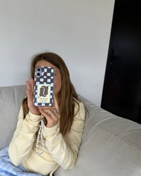 Klant houdt haar telefoon voor haar gezicht met hoesje Walk by faith, not by sight, met cowboylaarzen en een ruitjespatroon