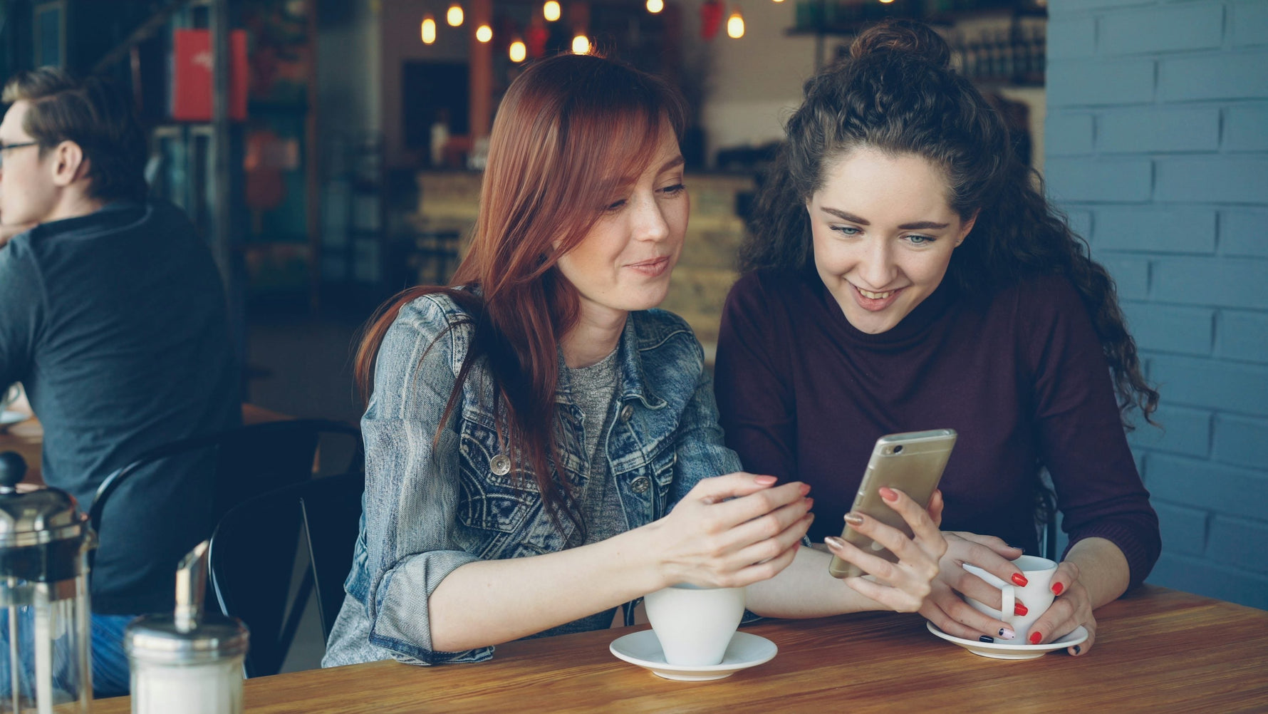 Twee vriendinnen die samen lachen naar een telefoon in een gezellig café