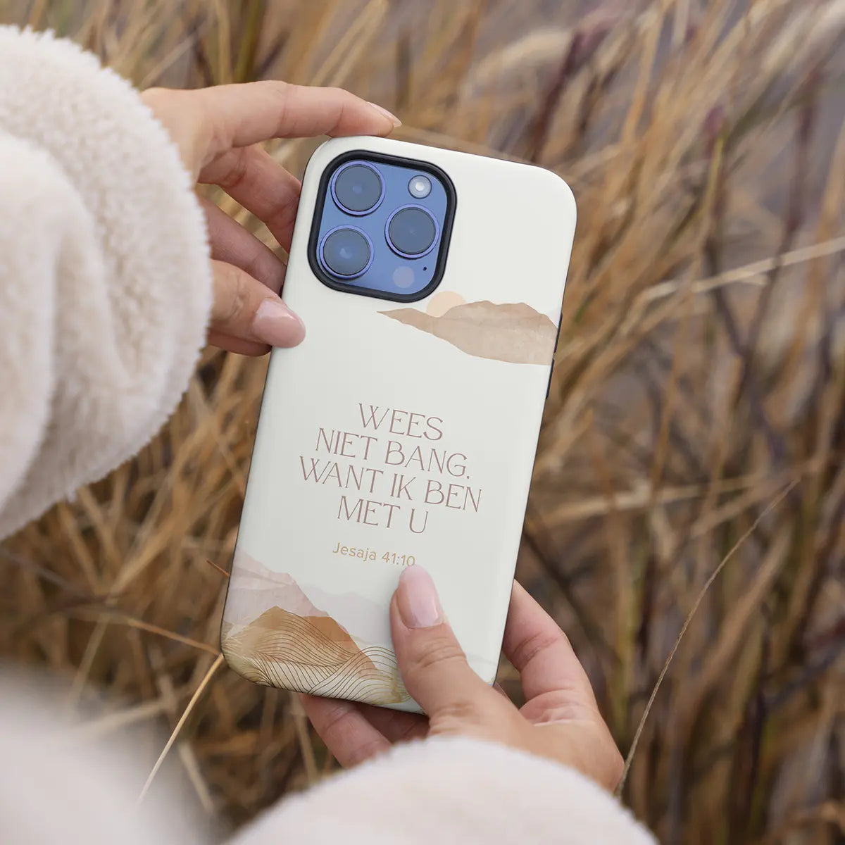 Vrouw houdt het Wees niet bang telefoonhoesje vast met riet op de achtergrond – duurzaam christelijk eco-hoesje geïnspireerd door Jesaja 41:10._sfeerbeeld