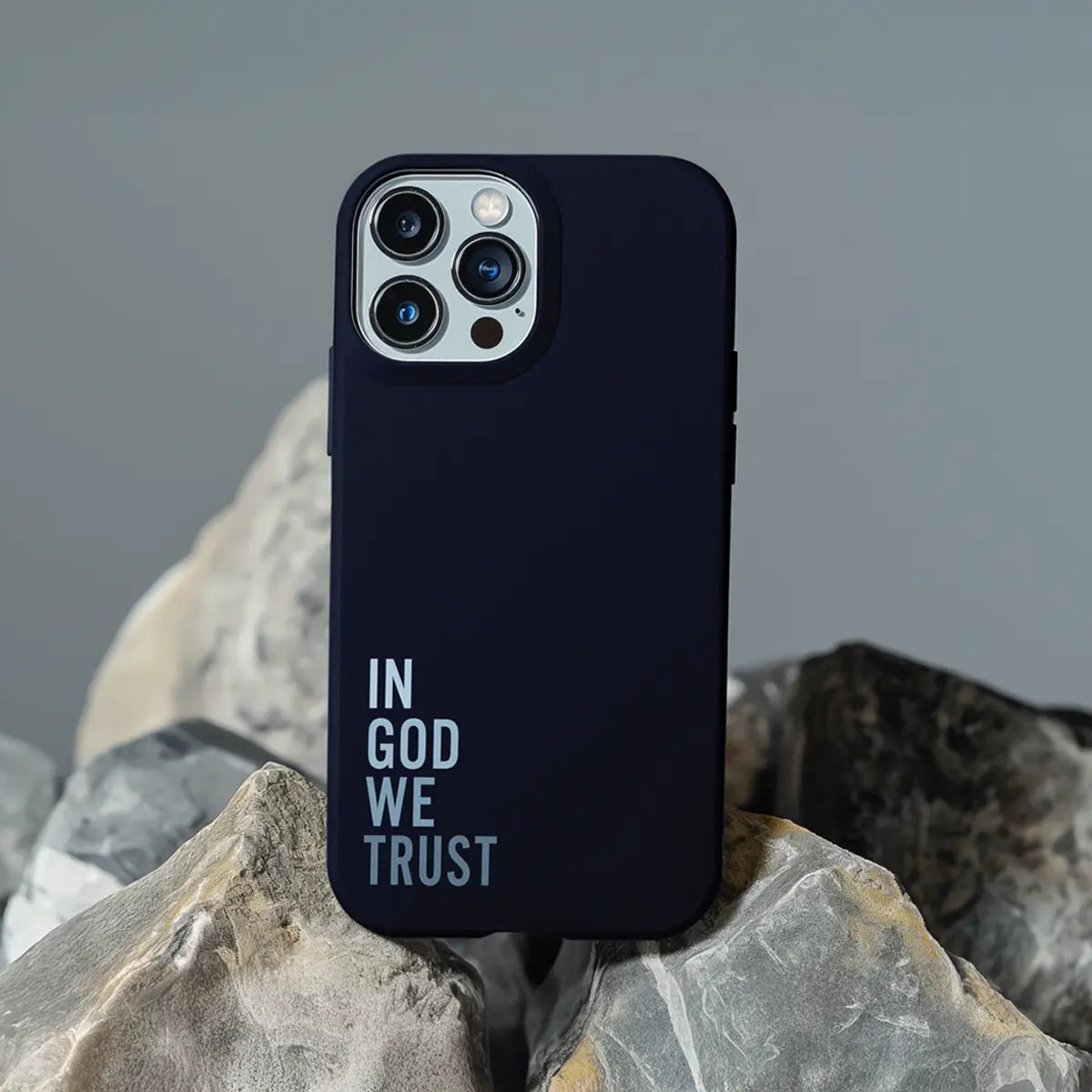 Stoer christelijk telefoonhoesje IN GOD WE TRUST op een rots, donkere achtergrond met witte letters en subtiele glow  hardcase uitvoering