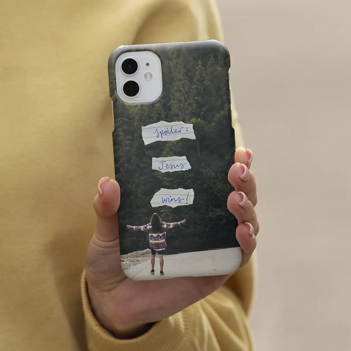 Mockup van christelijk telefoonhoesje Spoiler Jesus wins in handen van vrouw met bos op achtergrond