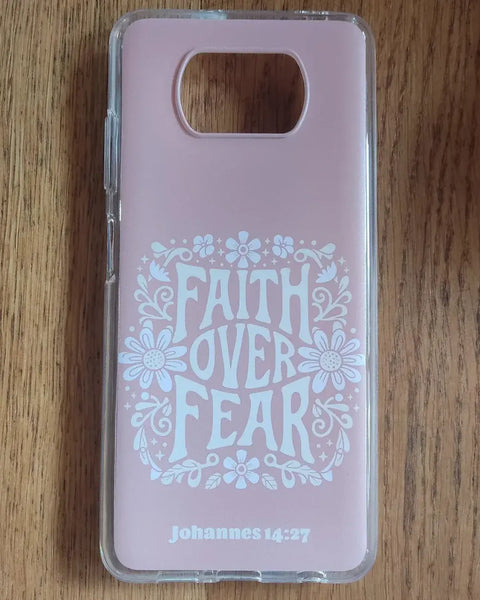 Roze christelijk telefoonhoesje Faith over Fear met witte bloemen en Johannes 14:27 op een houten tafel