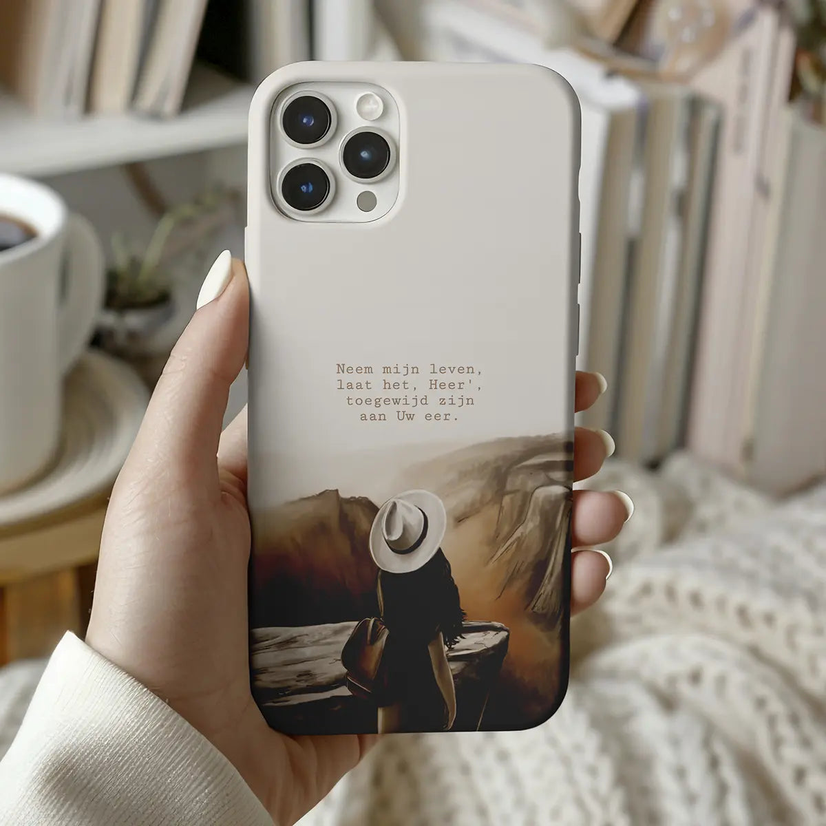 Christelijk softcase telefoonhoesje van Art by Claudia met artwork “Neem mijn leven – toegewijd aan Uw eer”, getoond in hand van vrouw zittend op de bank met koffie.